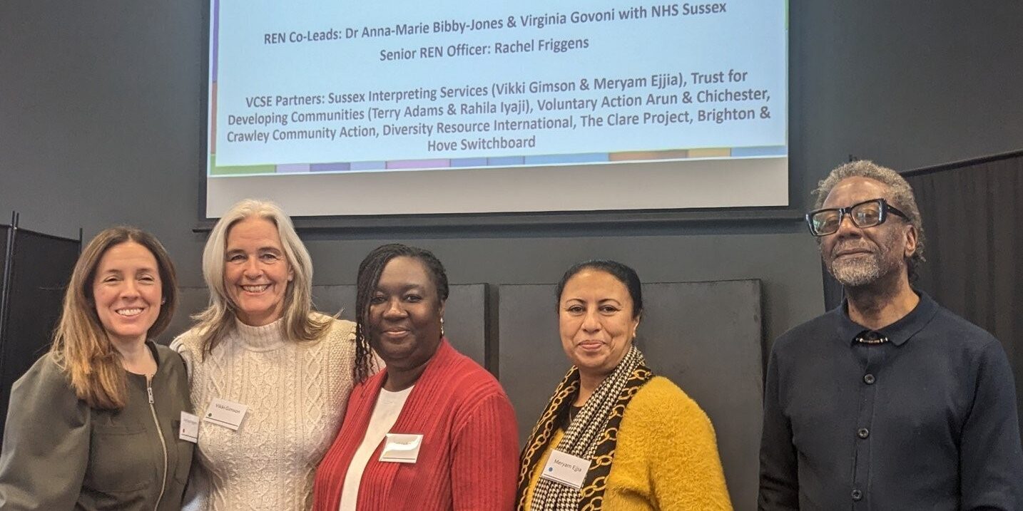 SE conference A group of five people smiling, underneath a projected slide showing information about the Sussex Research Engagement Network (REN)