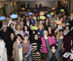 A large group of people smiling and waving and holding speech bubbles in many languages.