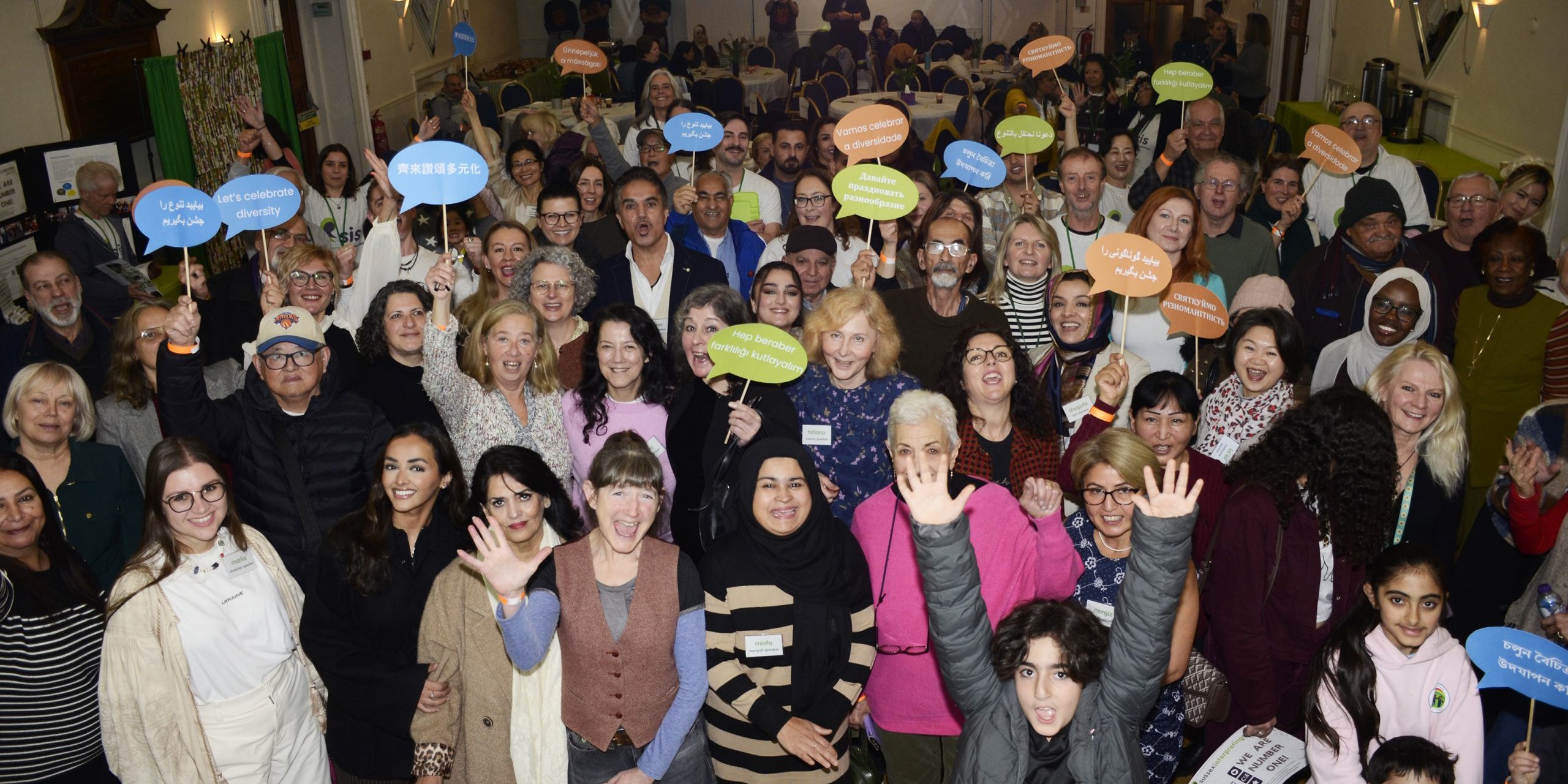 A large group of people smiling and waving and holding speech bubbles in many languages.