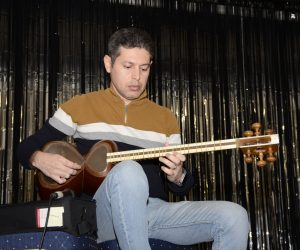 A man seated playing songs on the Tar, a long-necked, string instrument.